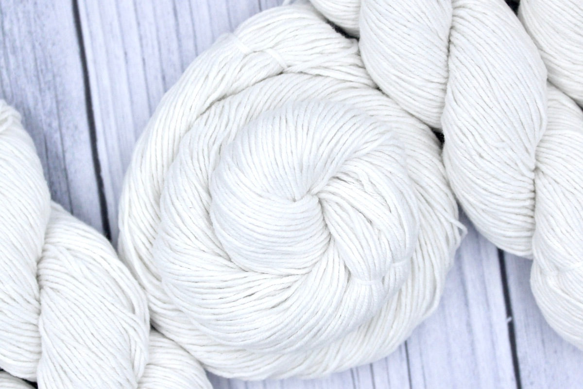 A skein of Pure White, Cotton, Fingering weight Yarn recycled by hand from unwanted sweaters swirled attractively in the center of the frame.