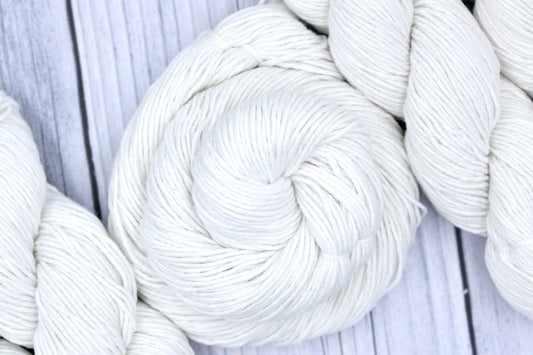 A skein of Pure White, Cotton, Fingering weight Yarn recycled by hand from unwanted sweaters swirled attractively in the center of the frame.