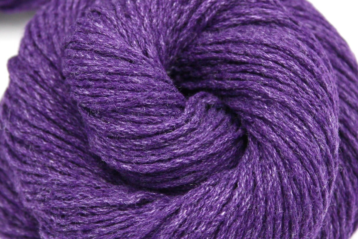 A close up shot of a skein of Eggplant Purple, Cotton, Acrylic, Dk weight Yarn recycled by hand from unwanted sweaters beautifully coiled in the center of the frame.