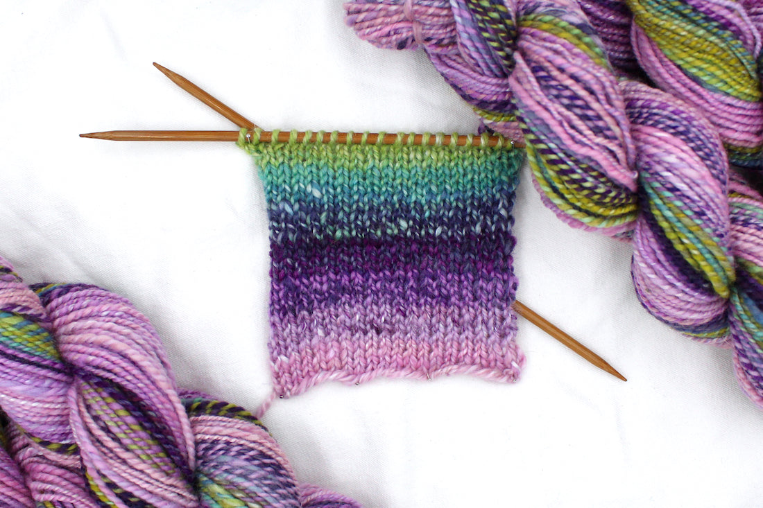 A sample swatch knitted on size 5 knitting needles from a one of a kind, Dk weight, hand dyed Gradient skein of multicolored Ballerina Pink, then move through Lavender, Magenta, Deep Purple, Baby Blue, Seafoam, and then finishes with Lime Green, Ombre self-striping Wool, and Mulberry Silk Yarn.