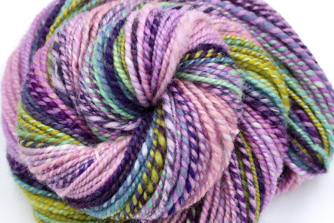 A close up view of a one of a kind, Dk weight, hand dyed Gradient skein of multicolored Ballerina Pink, then move through Lavender, Magenta, Deep Purple, Baby Blue, Seafoam, and then finishes with Lime Green, Ombre self-striping Wool, and Mulberry Silk Yarn.