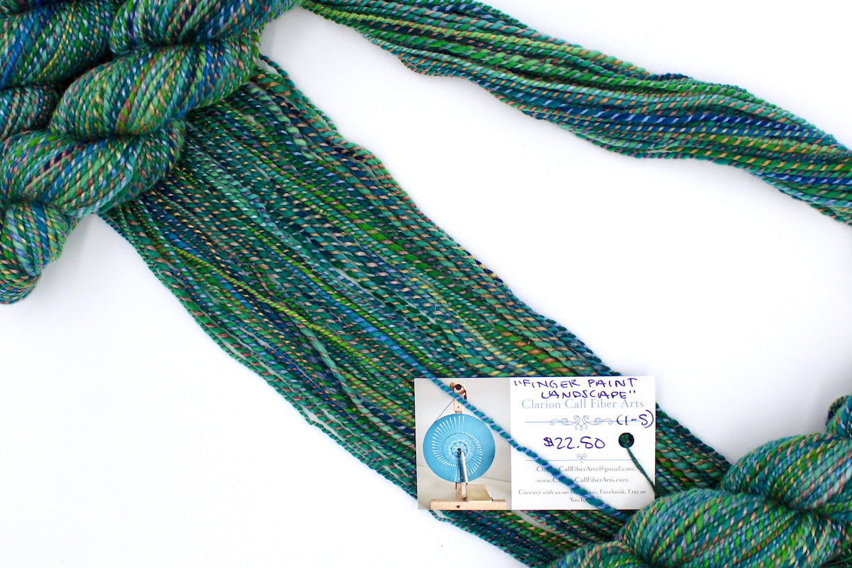 A one of a kind, hand dyed gradient skein of variegated skein of multicolored Green, Blue, Gold, and Red self-striping wool Yarn draped diagonally across the frame, so you can really see the color play.