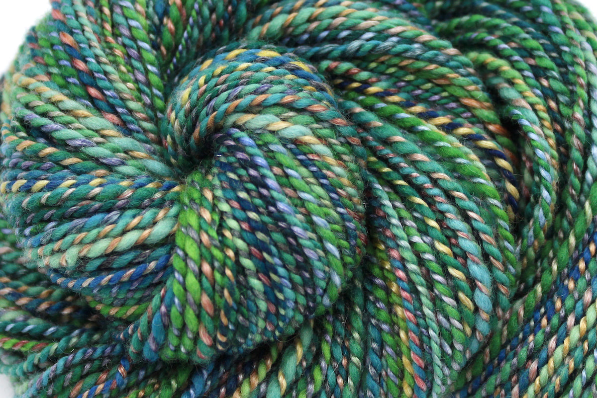 A close up view of a one of a kind, hand dyed variegated skein of multicolored Green, Blue, Gold, and Red self-striping wool Yarn.
