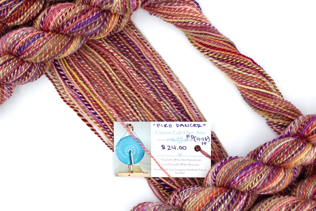 A one of a kind, hand dyed gradient skein of variegated skein of multicolored Orange, Pink, Yellow, and Purple self-striping wool Yarn draped diagonally across the frame, so you can really see the color play.