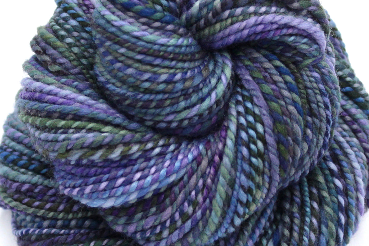 A close up view of a one of a kind, Dk Weight, hand dyed variegated skein of multicolored Purple, Lavender, Forest Green, Baby Blue, and Light Teal self-striping wool Yarn.