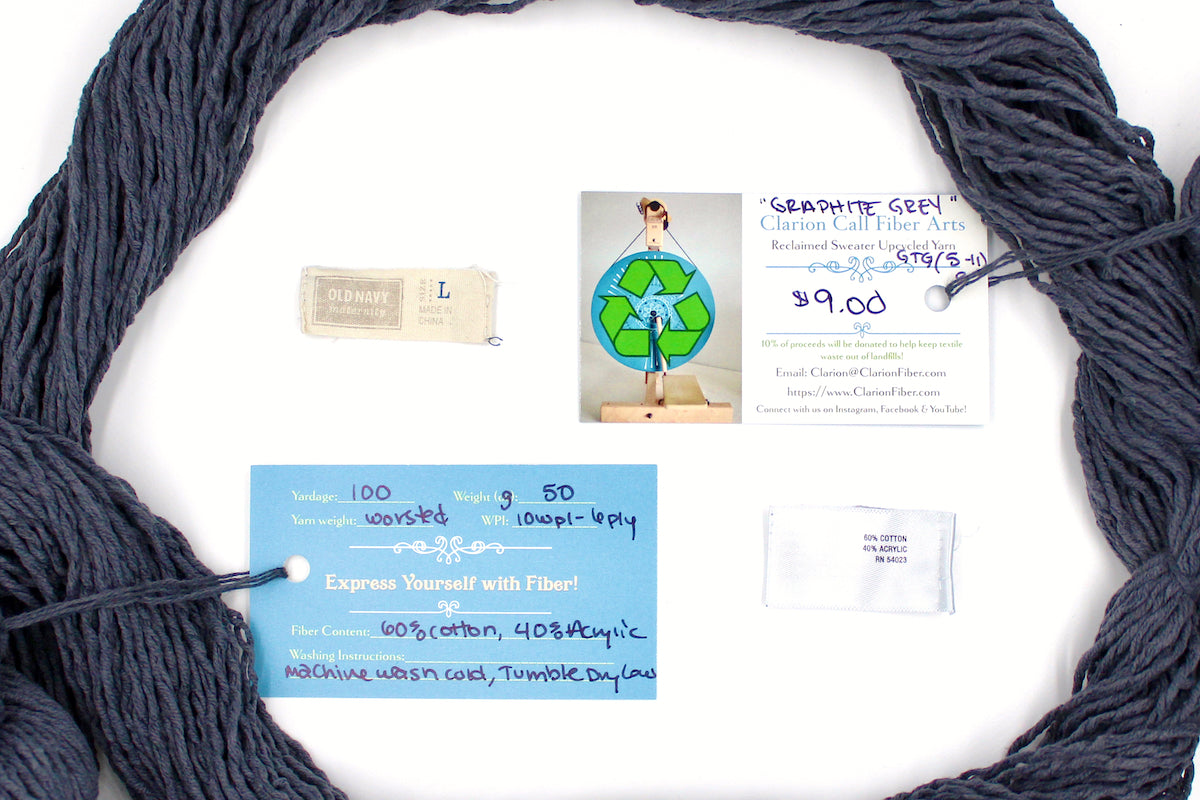 A skein of Vegan, Dark Grey, 60% Cotton, 40% Acrylic, Worsted Weight yarn encircling the sweater labels it was recycled from, as well as the hand written yarn tags detailing the specs of this recycled yarn to help you make your next project!
