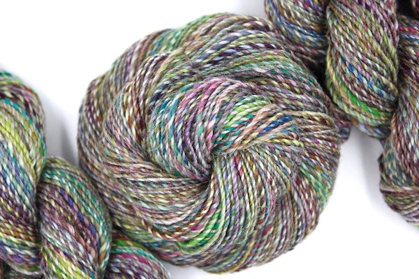 A one of a kind, hand dyed variegated skein of multicolored Navy, Maroon, Fuchsia, Teal, Kelly Green, Lime Green, and Gold self-striping wool Yarn coiled attractively in the center of the frame.