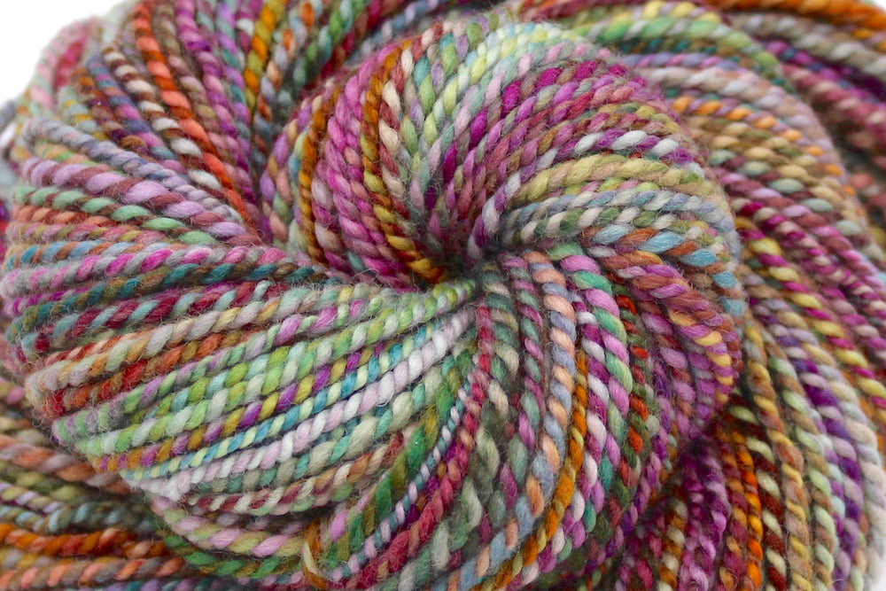 A close up view of a one of a kind, Worsted Weight, hand dyed variegated skein of multicolored Pink, Orange, Gold, Blue, Green, and Purple self-striping wool Yarn.