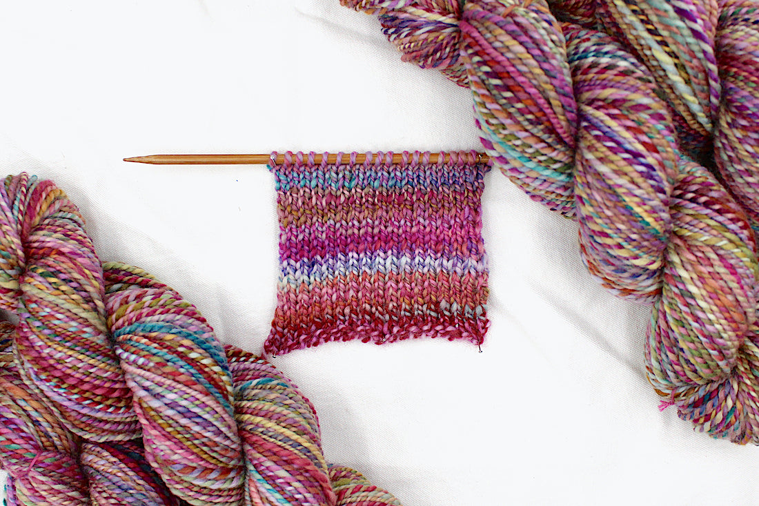 A sample swatch knitted from a one of a kind, Worsted weight, hand dyed variegated skein of multicolored Pink, Orange, Gold, Blue, Green, and Purple self-striping wool Yarn.