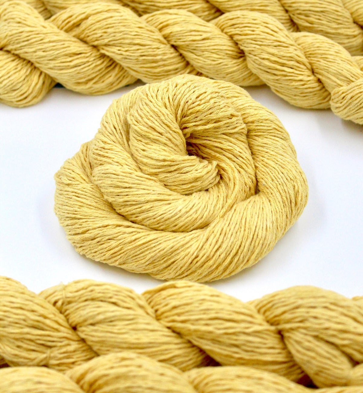 Several skeins of Golden Yellow, 100% Cotton, Sport weight recycled by hand from unwanted sweaters stacked on top of each other attractively.