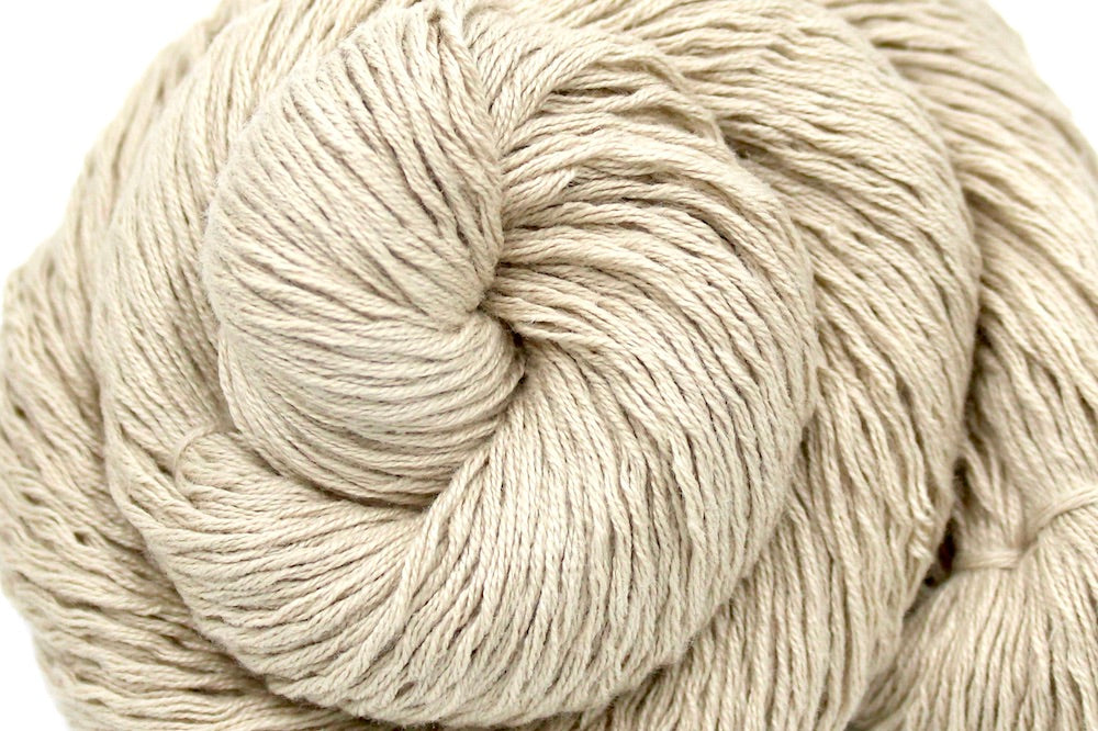 A close up shot of a skein of Vegan, Tan/ Beige/ Cream, Acrylic/ Cotton/ Nylon, Sport weight Yarn recycled by hand from unwanted sweaters beautifully coiled in the center of the frame.