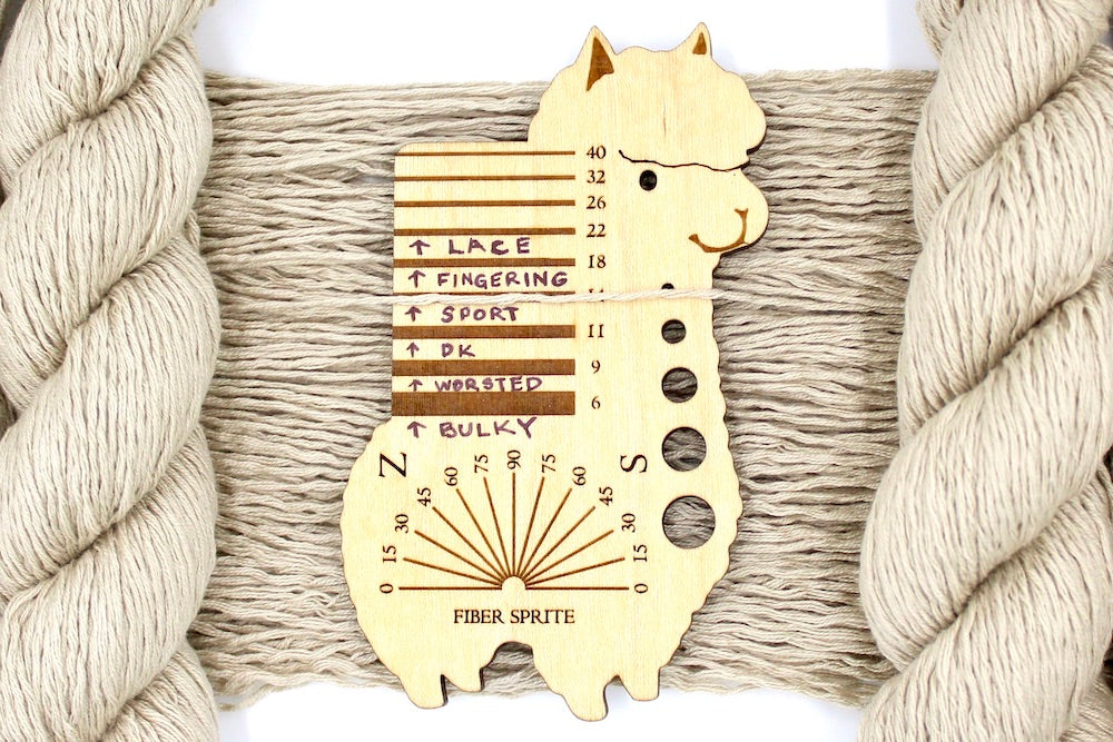 A skein of Vegan, Tan/ Beige/ Cream, Acrylic/ Cotton/ Nylon, Sport Weight Yarn recycled by hand from unwanted sweaters draped over a Llama shaped Yarn weight tool.
