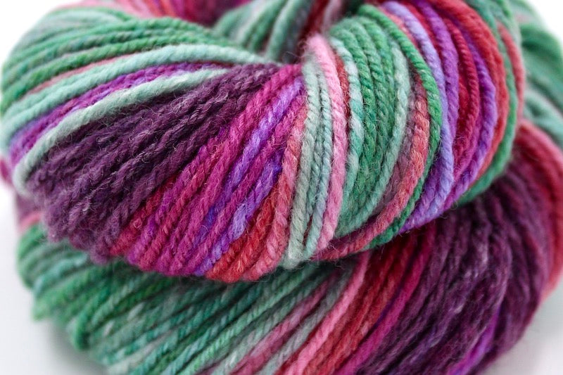 A close up view of a one of a kind, gradient skein of multicolored Plum Purple, Red, Fuchsia, Lavender, Pink, and Green self-striping wool Yarn.