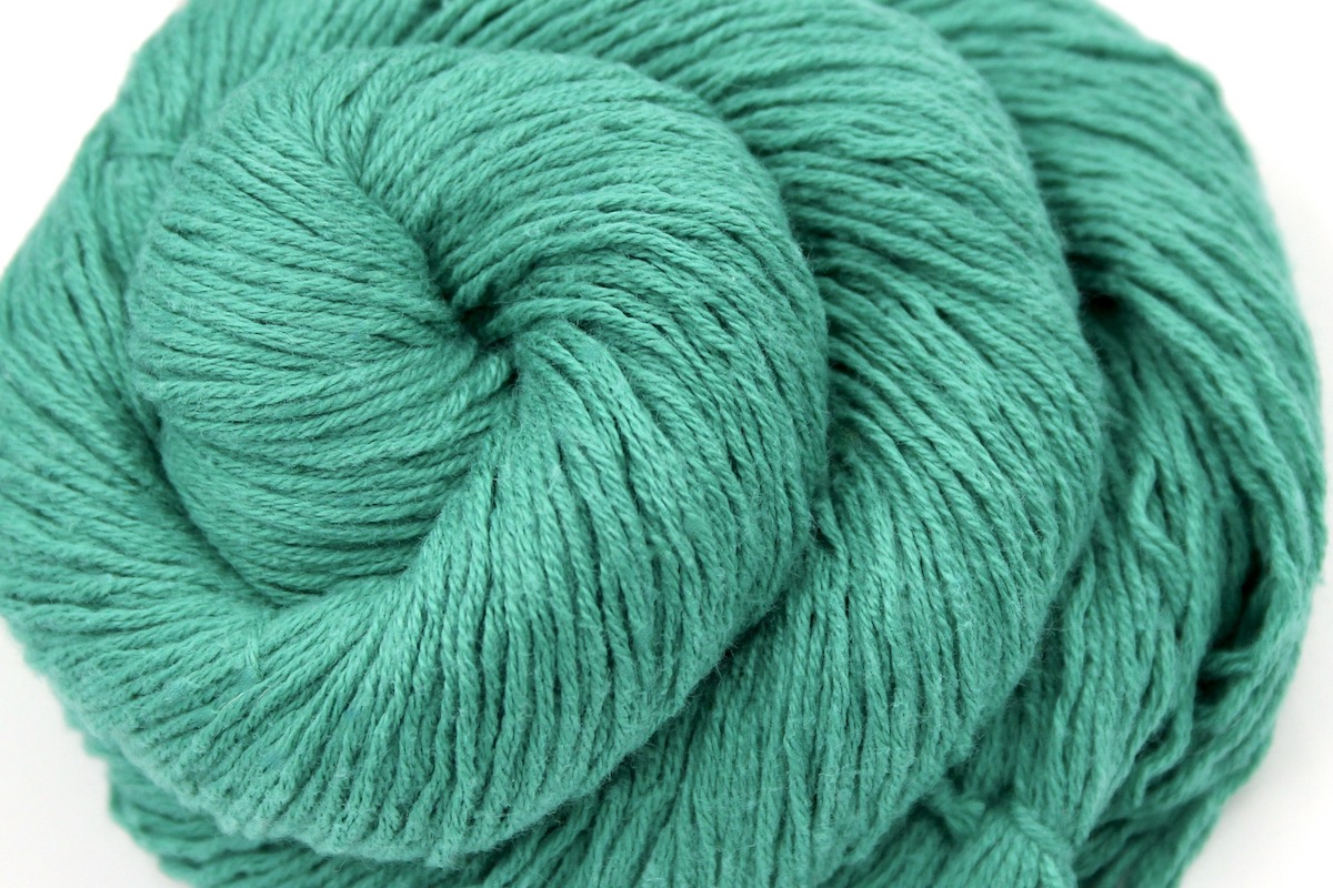 A close up shot of a skein of Vegan, Jungle Green, Cotton/ Acrylic, Fingering weight Yarn recycled by hand from unwanted sweaters beautifully coiled in the center of the frame.