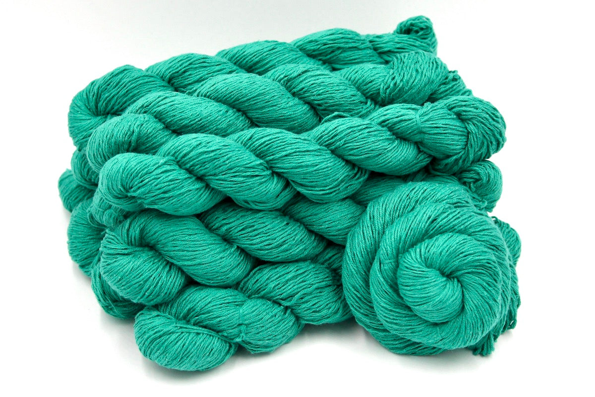 Several skeins of Vegan, Vegan, Jungle Green, Cotton/ Acrylic, Fingering weight recycled by hand from unwanted sweaters stacked on top of each other attractively.