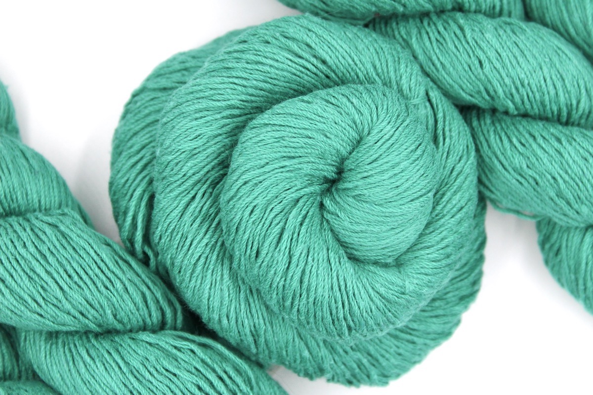 A skein of Vegan, Jungle Green, Cotton/ Acrylic, Fingering weight Yarn recycled by hand from unwanted sweaters swirled attractively in the center of the frame.
