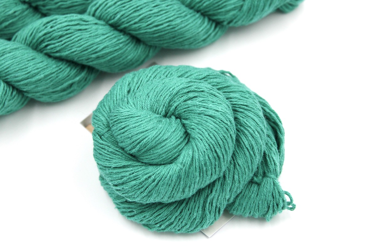 A skein of Vegan, Jungle Green, Cotton/ Acrylic, Fingering weight Yarn recycled by hand from unwanted sweaters swirled attractively in the center of the frame.