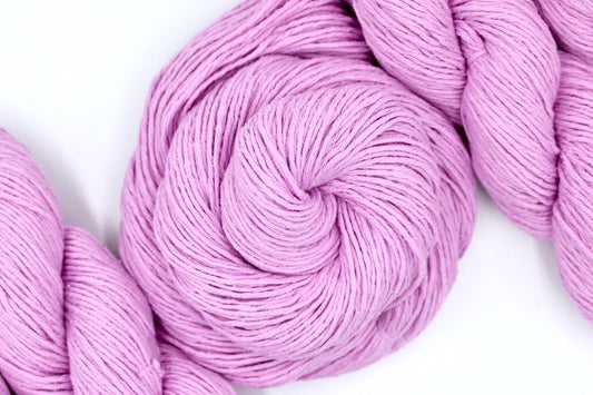 A skein of Vegan, Pastel Pink, 100% Cotton, Sport weight Yarn recycled by hand from unwanted sweaters swirled attractively in the center of the frame.