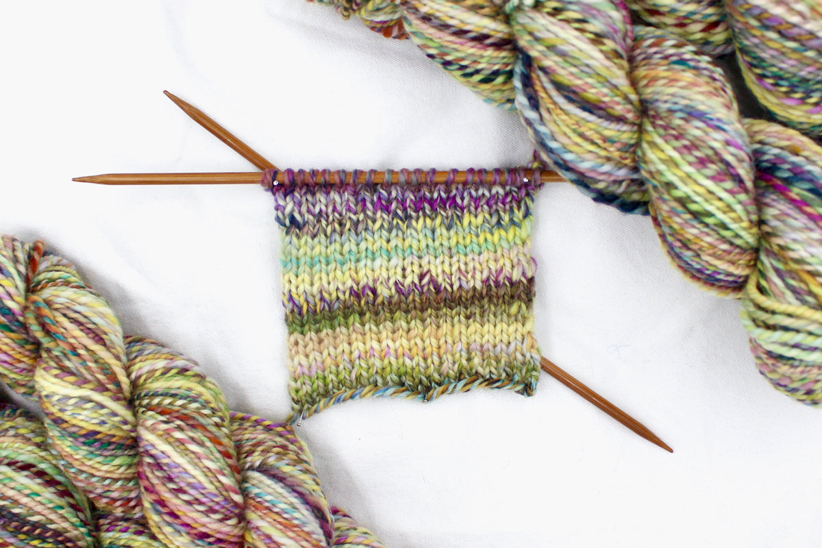 A sample swatch knitted from a one of a kind, Worsted weight, hand dyed variegated skein of multicolored Green, Maroon, Pink, Yellow and Chartreuse, self-striping superwash wool Yarn.
