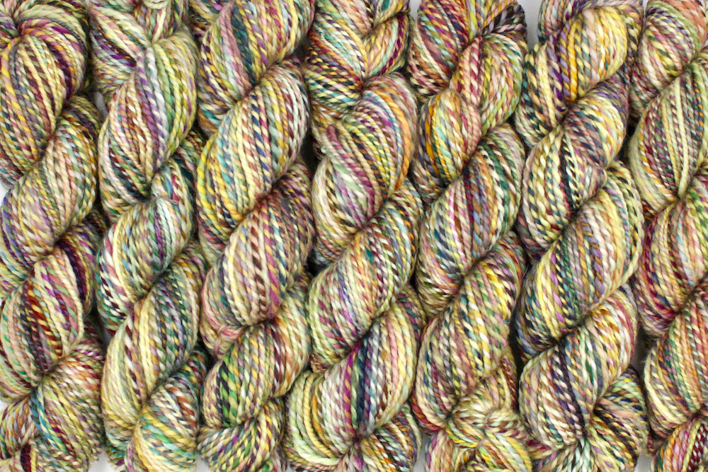 Six one of a kind, Worsted weight, hand dyed variegated skein of multicolored Green, Maroon, Pink, Yellow and Chartreuse, self-striping superwash wool Yarn lined up side by side.