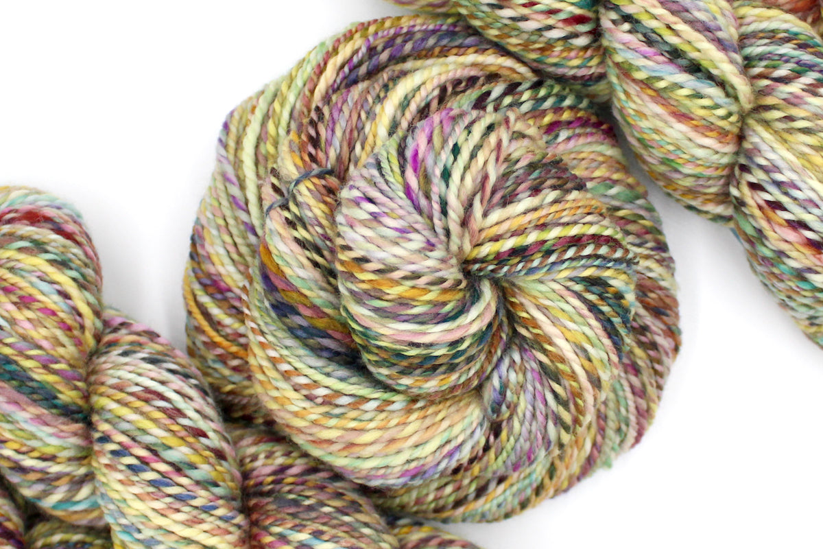 A one of a kind, Worsted Weight, hand dyed variegated skein of multicolored Green, Maroon, Pink, Yellow and Chartreuse, self-striping superwash wool Yarn coiled attractively in the center of the frame.