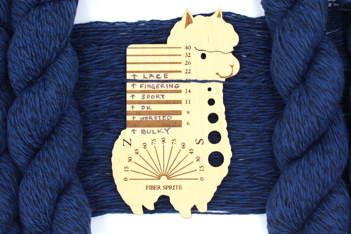 A skein of Vegan, Navy Blue/ Black, Cotton/ Acrylic, Fingering Weight Yarn recycled by hand from unwanted sweaters draped over a Llama shaped Yarn weight tool.