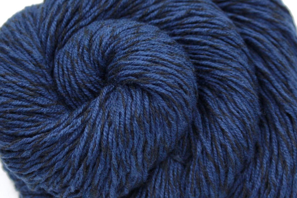 A close up shot of a skein of Vegan, Navy Blue/ Black, Cotton/ Acrylic, Fingering weight Yarn recycled by hand from unwanted sweaters beautifully coiled in the center of the frame.