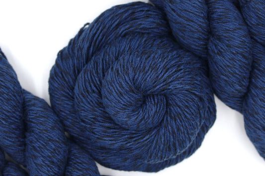 A skein of Vegan, Navy Blue/ Black, Cotton/ Acrylic, Fingering weight Yarn recycled by hand from unwanted sweaters swirled attractively in the center of the frame.