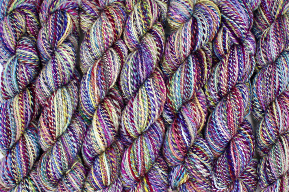 Six one of a kind, Sport Weight, hand dyed variegated skein of multicolored Rainbow self-striping 100% Superwash Merino wool Yarn lined up side by side.