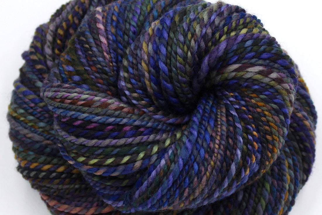 A close up view of a one of a kind, Worsted Weight, hand dyed variegated skein of multicolored Blue, Purple, Yellow, and Olive Green, and Maroon self-striping wool Yarn.