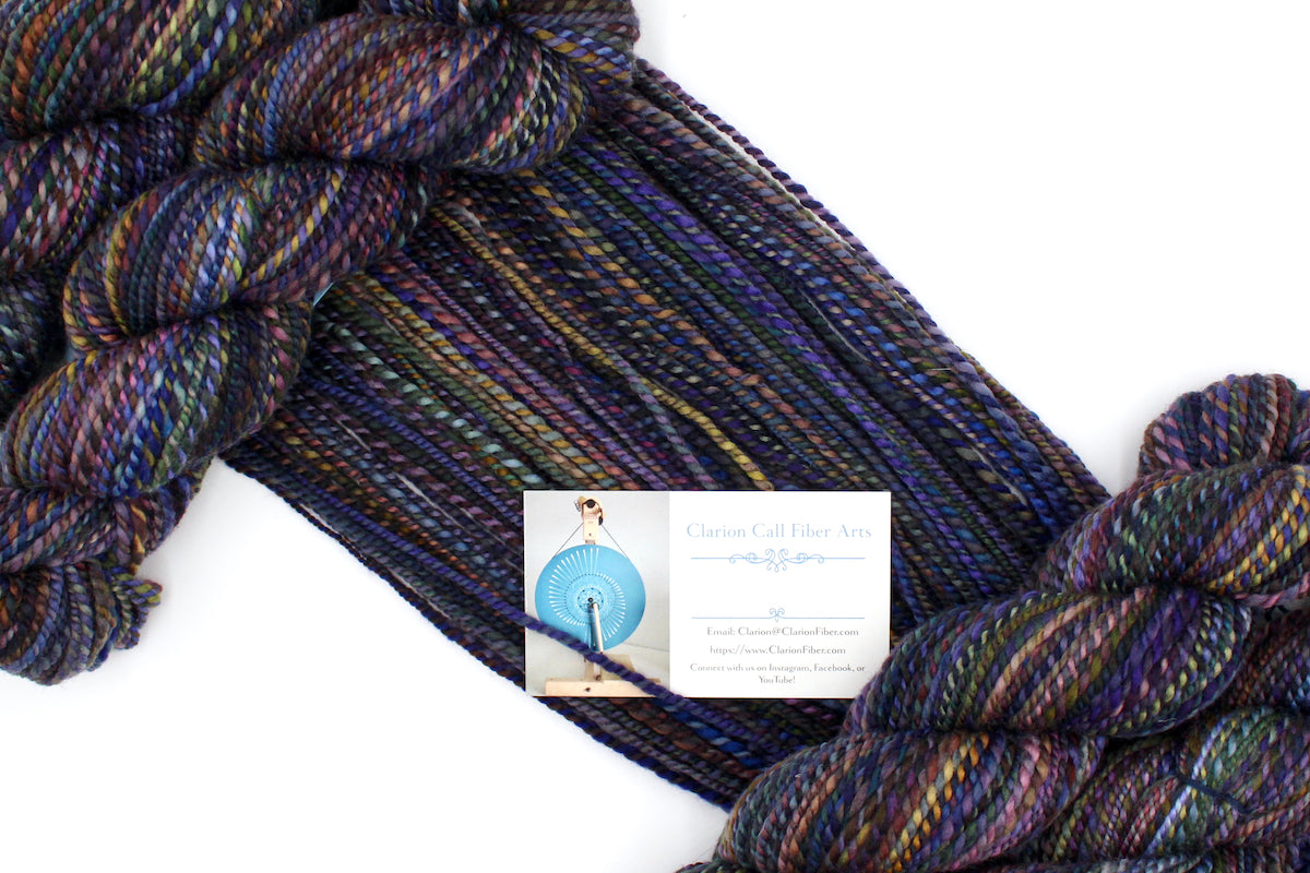 A one of a kind, Worsted weight, hand dyed variegated skein of multicolored Blue, Purple, Yellow, and Olive Green, and Maroon self-striping wool Yarn draped diagonally across the frame, so you can really see the color play.