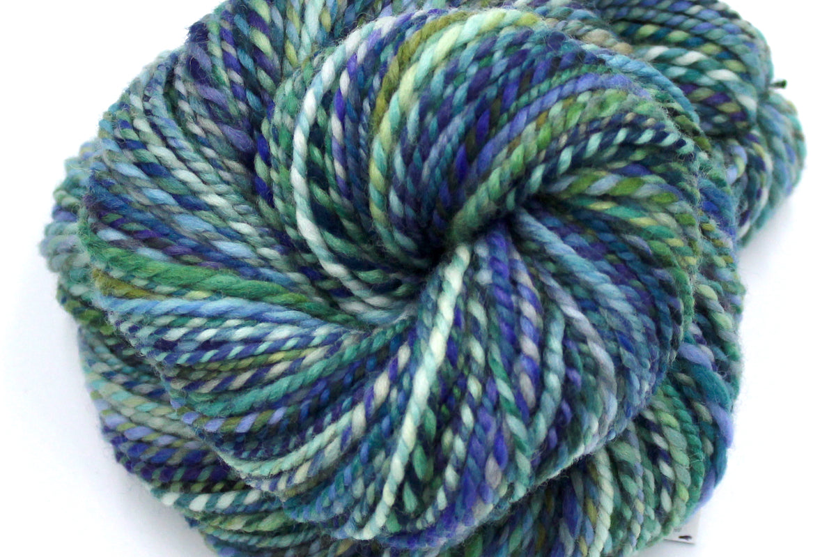A close up view of a one of a kind, Worsted Weight, hand dyed variegated skein of multicolored Blue, Green, Teal, Light and Yellow, self-striping wool Yarn.