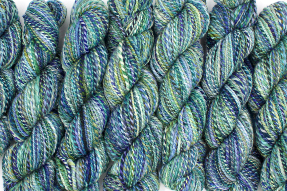 Six one of a kind, Worsted weight, hand dyed variegated skein of multicolored Blue, Green, Teal, and Light Yellow, self-striping wool Yarn lined up side by side.