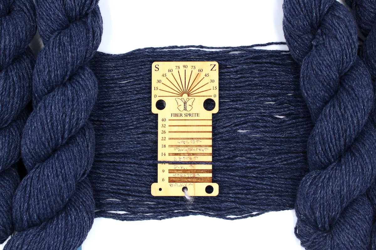 A skein of Vegan, Slate Navy Blue, Cotton/ Acrylic, Dk Weight Yarn recycled by hand from unwanted sweaters draped over a Llama shaped Yarn weight tool.