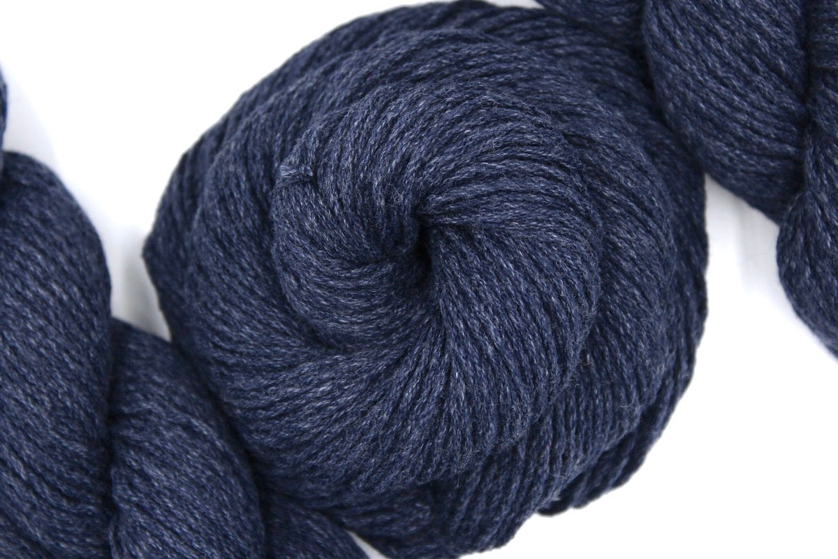 A skein of Vegan, Slate Navy Blue, Cotton/ Acrylic, Dk weight Yarn recycled by hand from unwanted sweaters swirled attractively in the center of the frame.