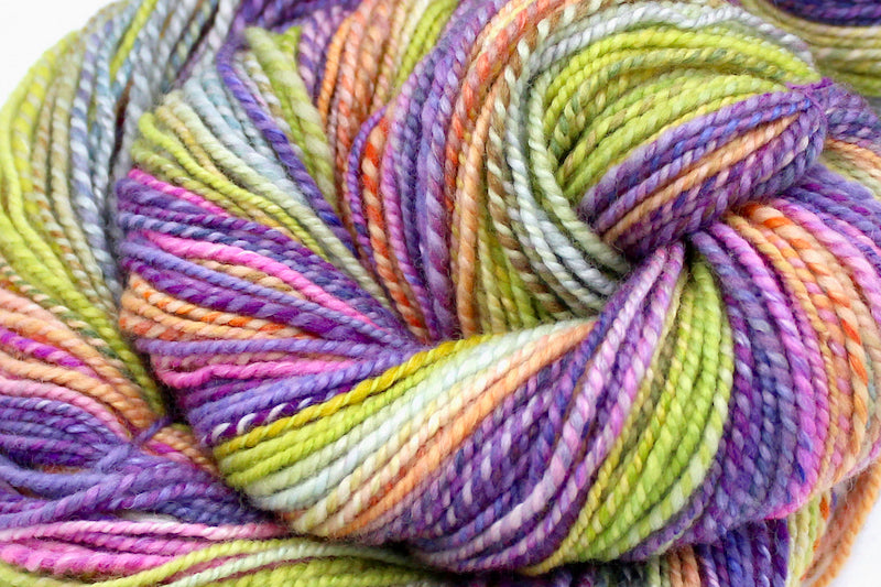 A close up view of a one of a kind, gradient skein of multicolored Purple, Neon Pink, Orange, Yellow Neon Green, and Light Blue self-striping wool Yarn.