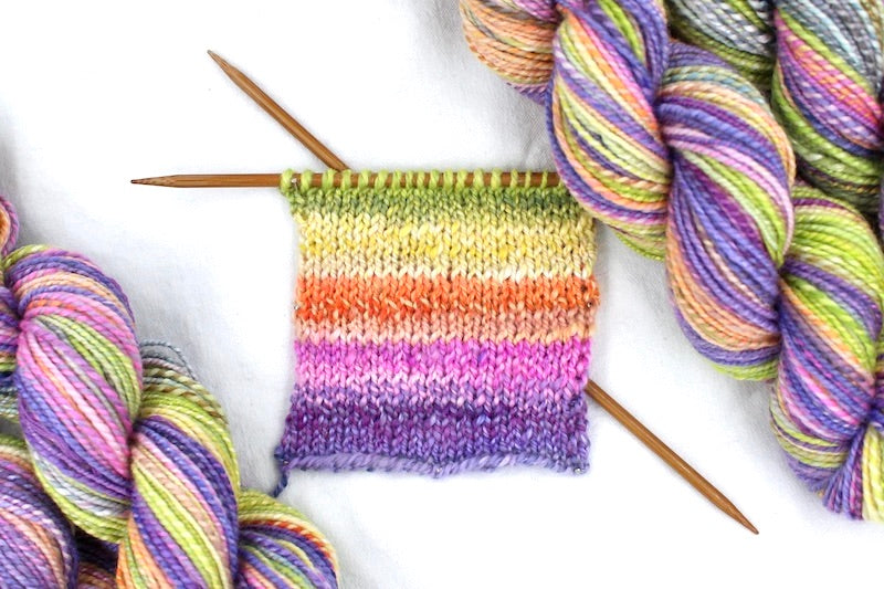 A sample swatch knitted from a one of a kind, hand dyed gradient skein of multicolored Purple, Neon Pink, Orange, Yellow Neon Green, and Light Blue self-striping wool Yarn.
