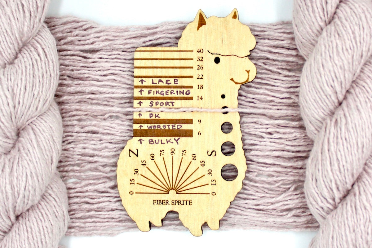 A skein of Vegan, Light Pastel Pink, Cotton/ Acrylic/ Polyester, Dk Weight Yarn recycled by hand from unwanted sweaters draped over a Llama shaped Yarn weight tool.