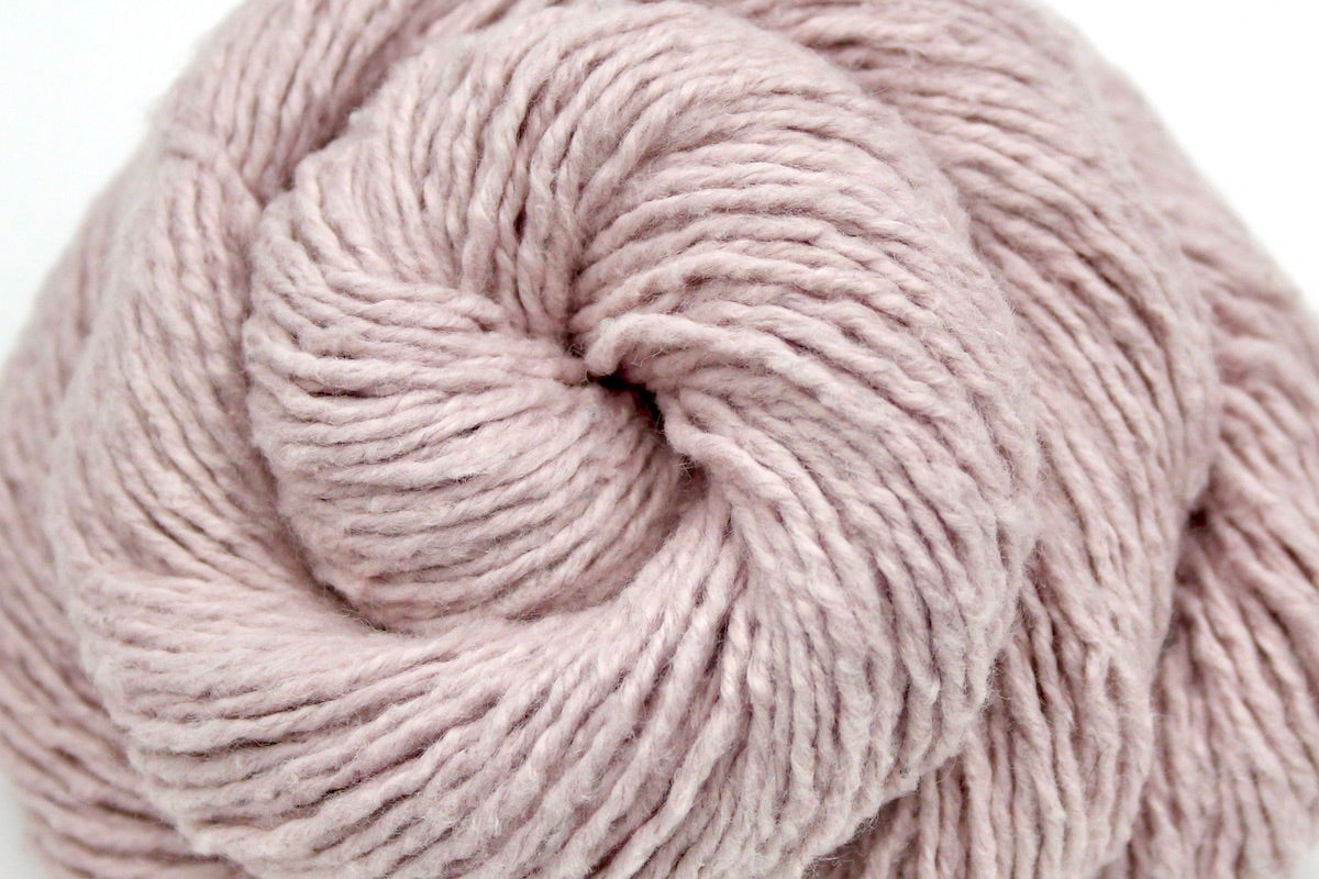 A close up shot of a skein of Vegan, Light Pastel Pink, Cotton/ Acrylic/ Polyester, Dk weight Yarn recycled by hand from unwanted sweaters beautifully coiled in the center of the frame.