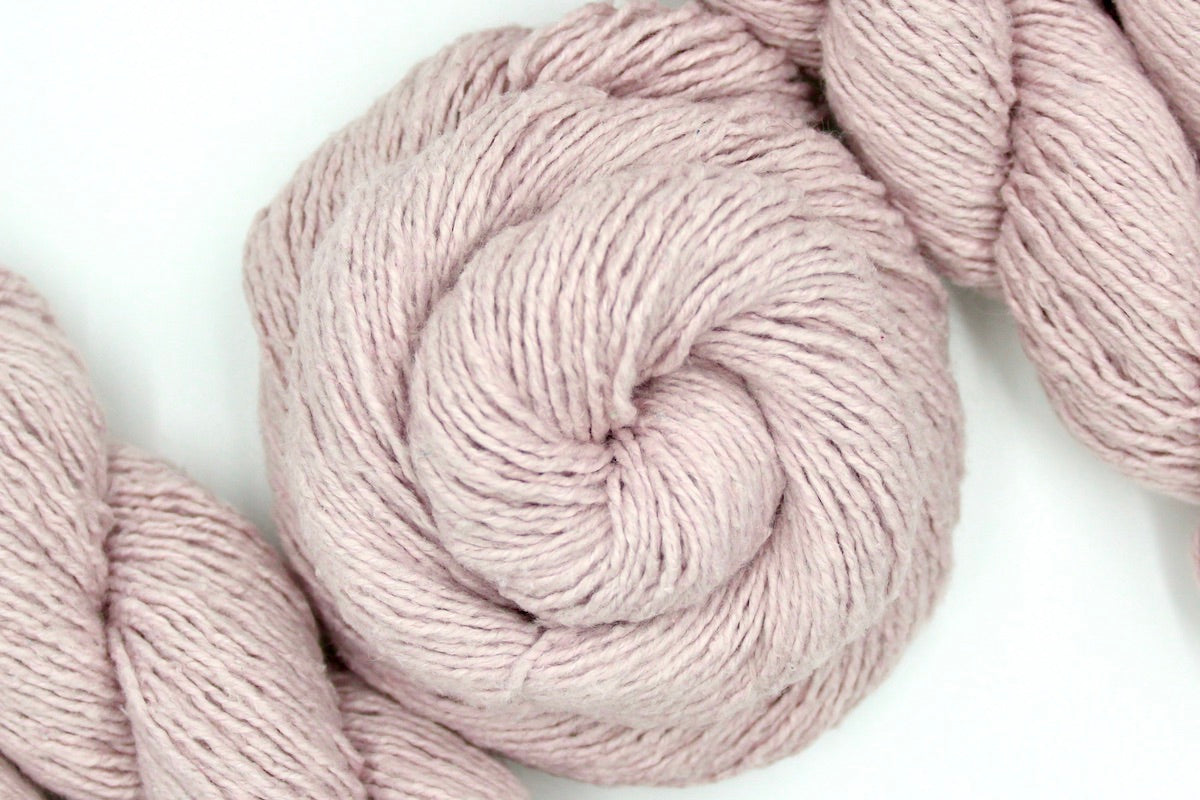 A skein of Vegan, Light Pastel Pink, Cotton/ Acrylic/ Polyester, Dk weight Yarn recycled by hand from unwanted sweaters swirled attractively in the center of the frame.