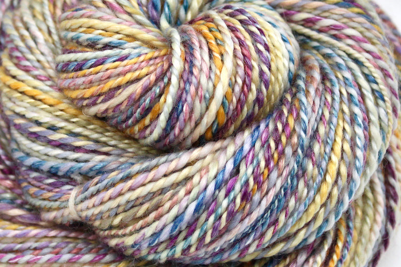 A close up view of a one of a kind, variegated skein of multicolored Purple, Pink, Blue, Yellow and Orange self-striping wool Yarn.