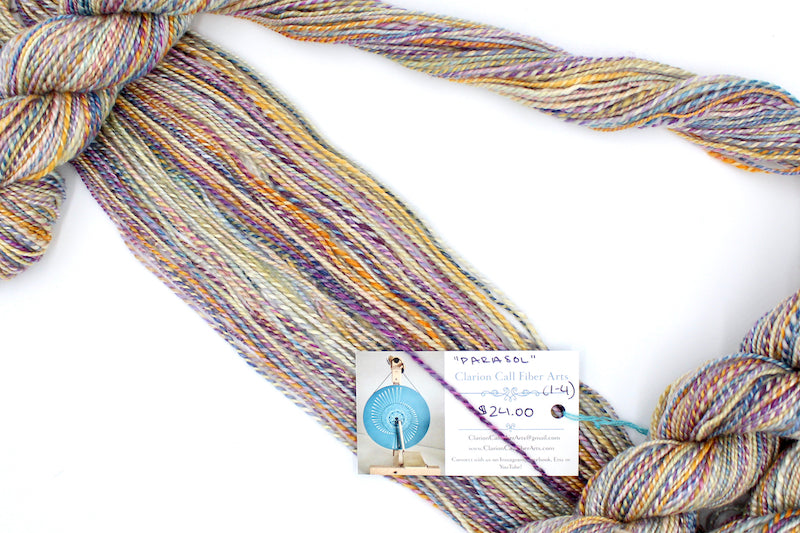 A one of a kind, hand dyed variegated skein of multicolored Purple, Pink, Blue, Yellow and Orange self-striping wool Yarn draped diagonally across the frame, so you can really see the color play.