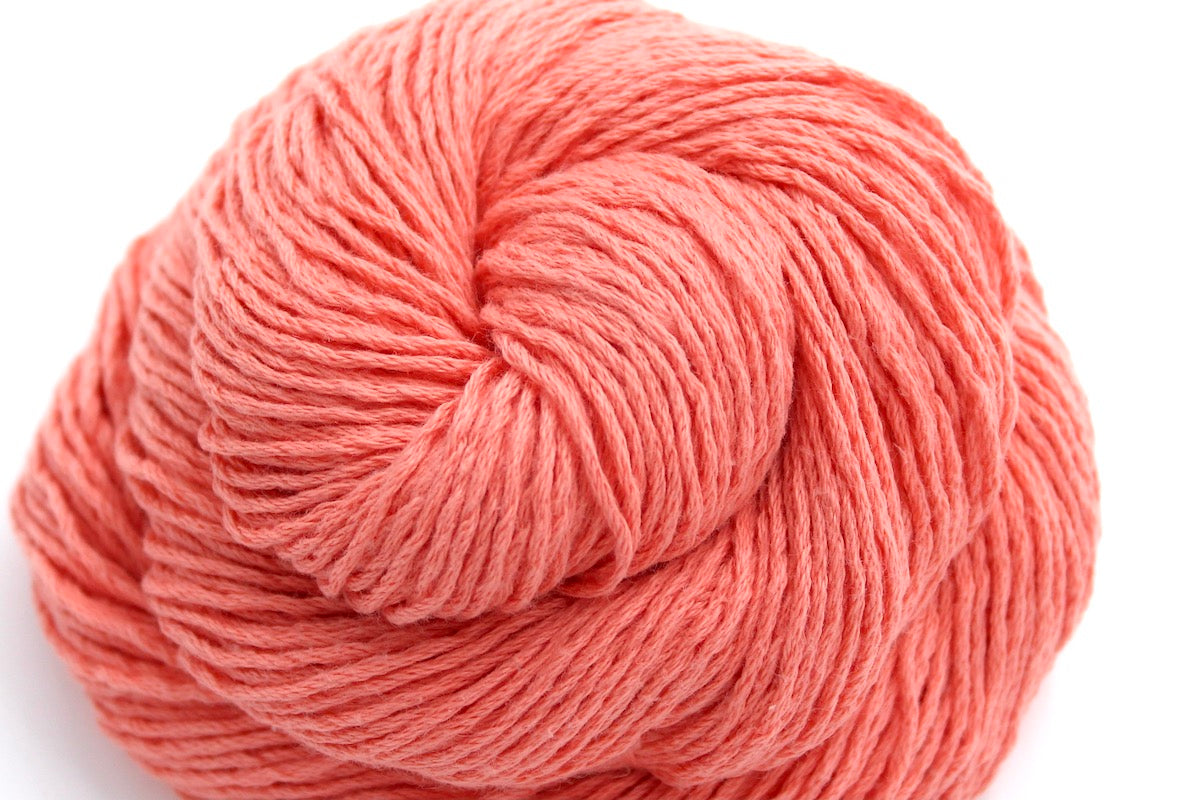 A close up shot of a skein of Vegan, Neon Peach, 100% Cotton, Sport weight Yarn recycled by hand from unwanted sweaters beautifully coiled in the center of the frame.