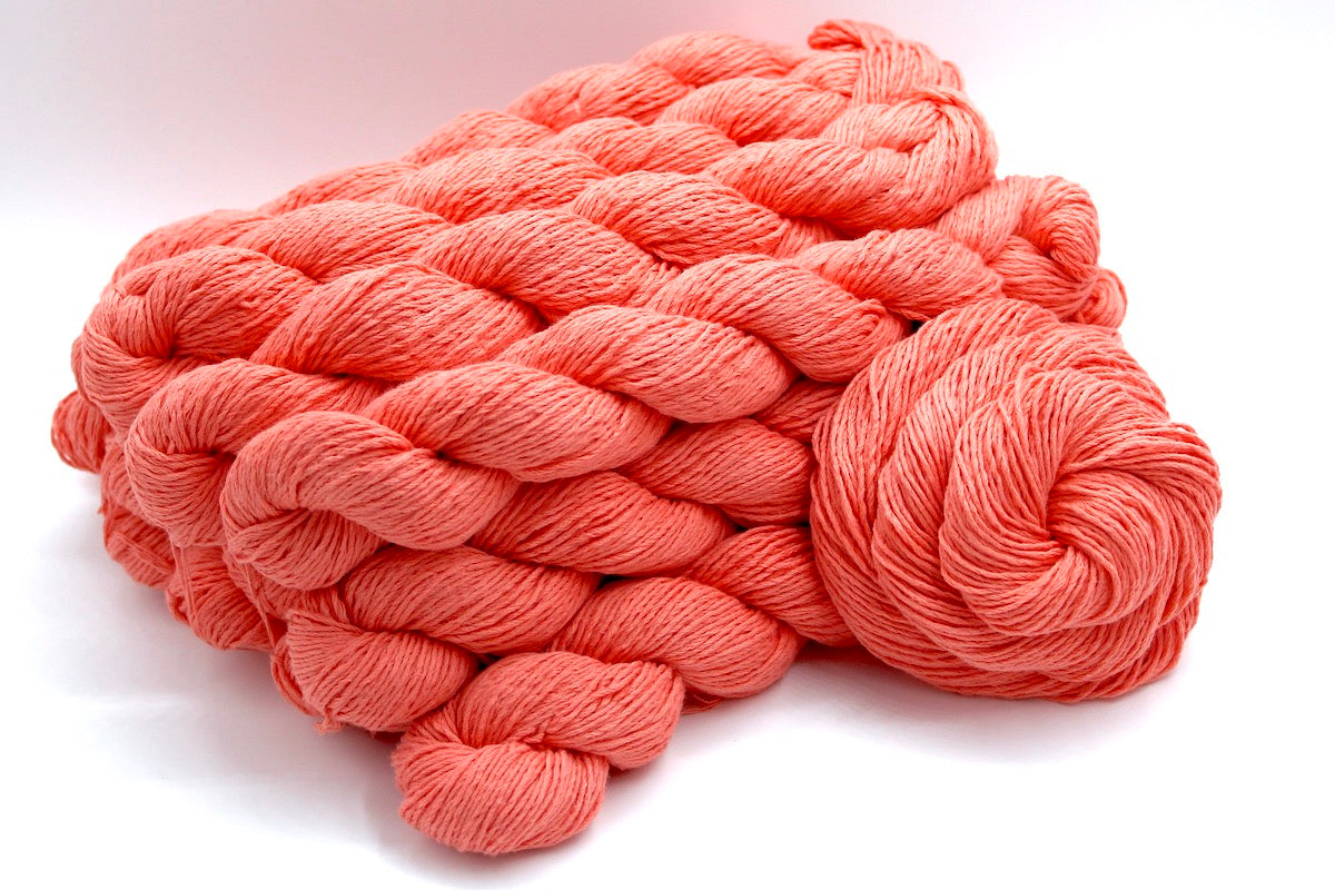 Several skeins of Vegan, Bright Peach, 100% Cotton, Sport weight recycled by hand from unwanted sweaters stacked on top of each other attractively.