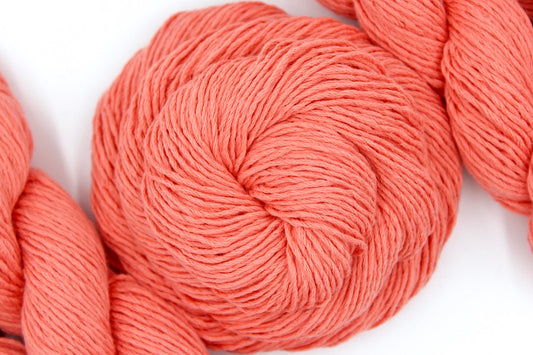 A skein of Vegan, Neon Peach, 100% Cotton, Sport weight Yarn recycled by hand from unwanted sweaters swirled attractively in the center of the frame.