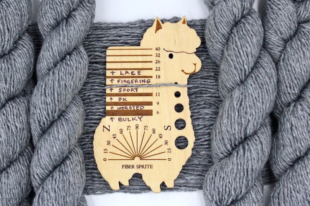 A skein of Silver Grey, Acrylic/ Nylon/ Wool, Sport Weight Yarn recycled by hand from unwanted sweaters draped over a Llama shaped Yarn weight tool.