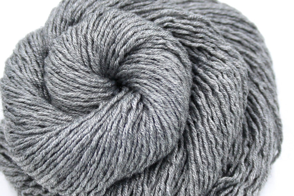 A close up shot of a skein of Silver Grey, Acrylic/ Nylon/ Wool, Sport weight Yarn recycled by hand from unwanted sweaters beautifully coiled in the center of the frame.