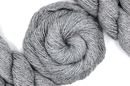 A skein of Silver Grey, Acrylic/ Nylon/ Wool, Sport weight Yarn recycled by hand from unwanted sweaters swirled attractively in the center of the frame.