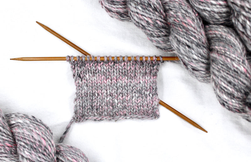 A sample swatch knitted from a one of a kind, hand dyed variegated skein of multicolored Grey, White, and Pink self-striping wool Yarn.