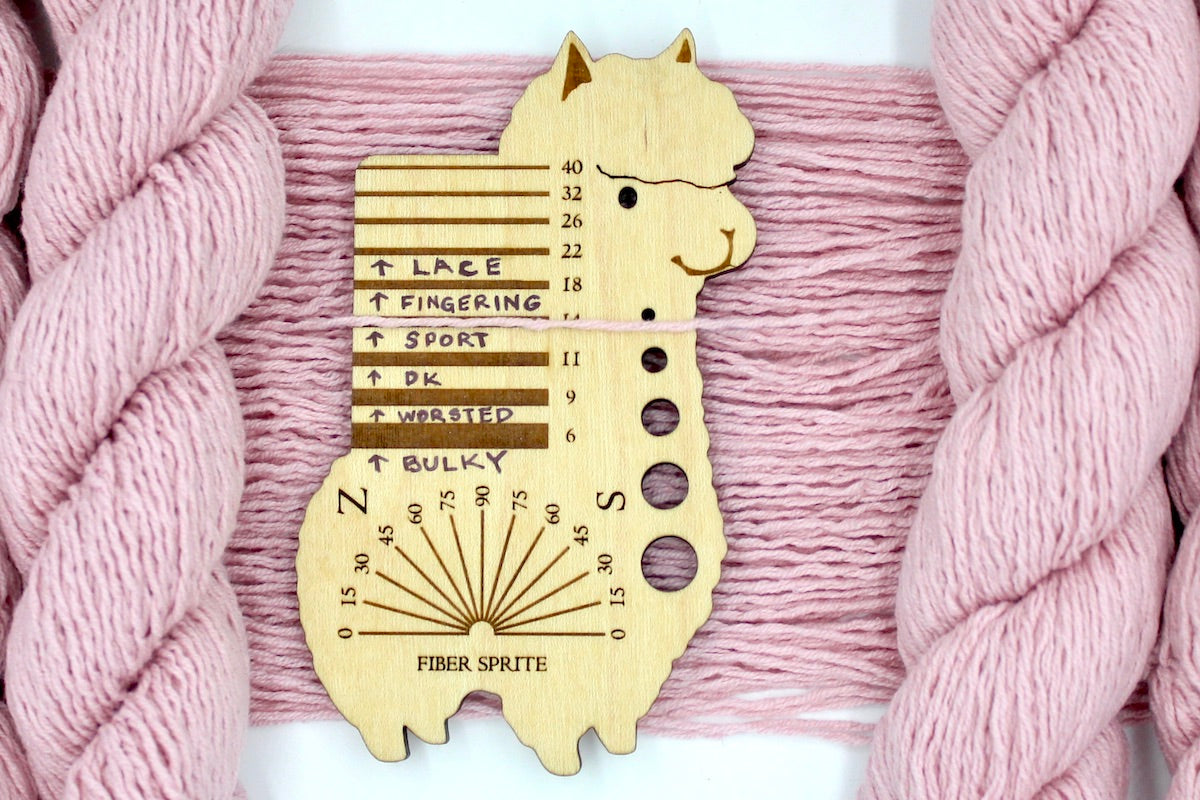 A skein of Vegan, Light Ballet Pink, Cotton/ Acrylic, Sport Weight Yarn recycled by hand from unwanted sweaters draped over a Llama shaped Yarn weight tool.